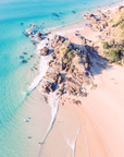 Aerial view of The Pass, Byron Bay showing rocky point with stairs, sand beach and shallow waves along a curved shoreline