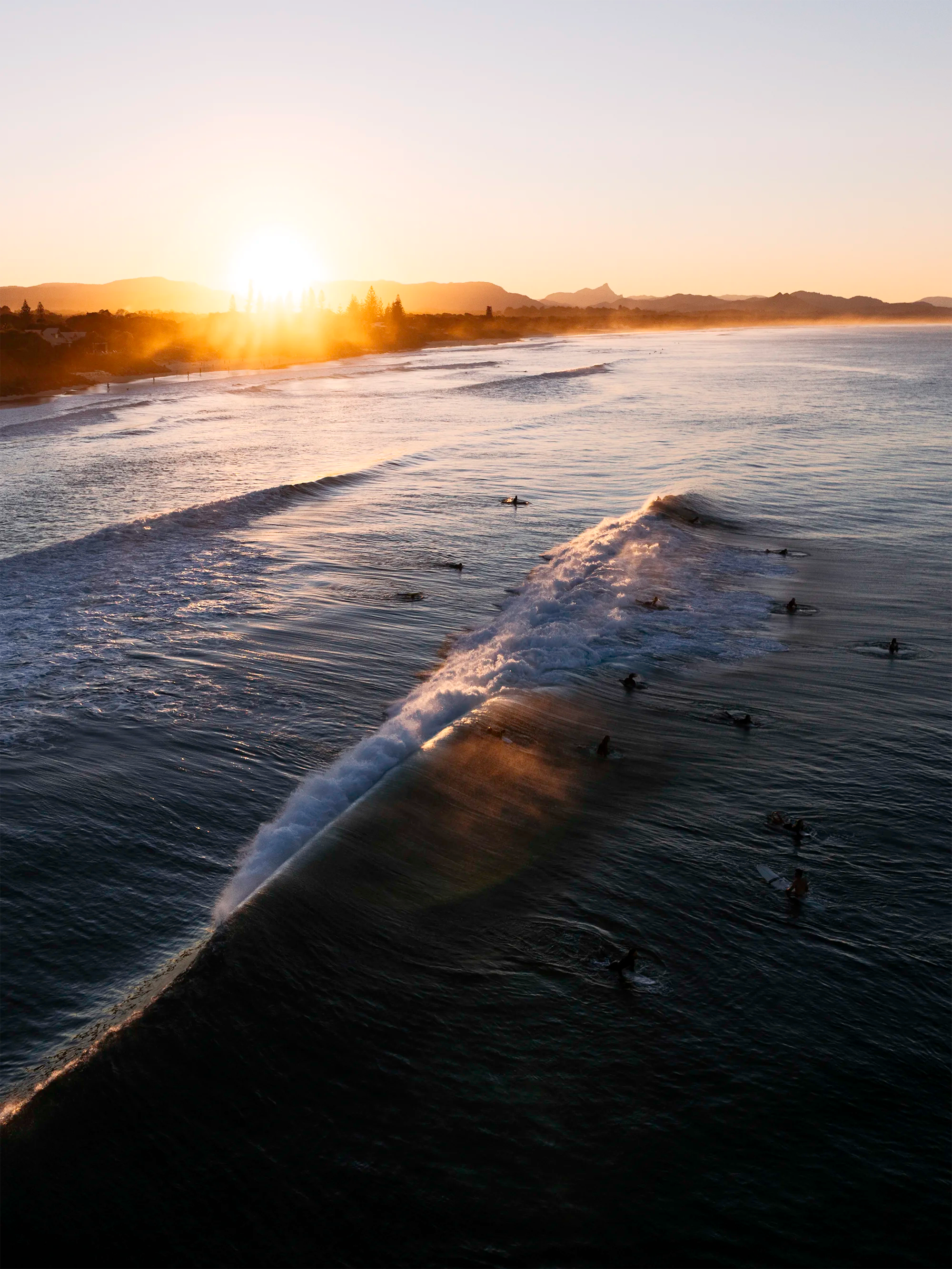 Belongil Beach, Byron Bay wave breaking with surfers sitting and paddling along the lineup in low sunset light
