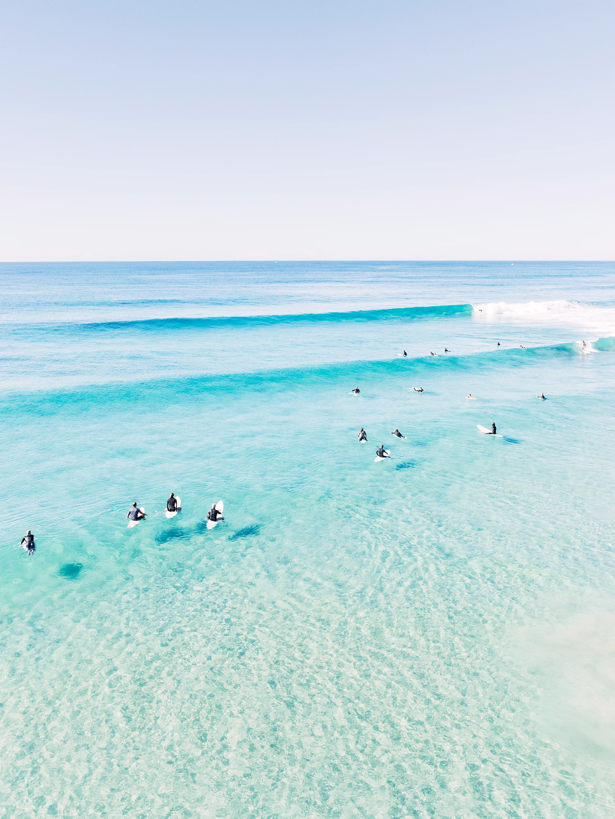 Surfers in a shallow surf lineup at Second Bay, Coolum with clean wave lines forming across clear water over sand