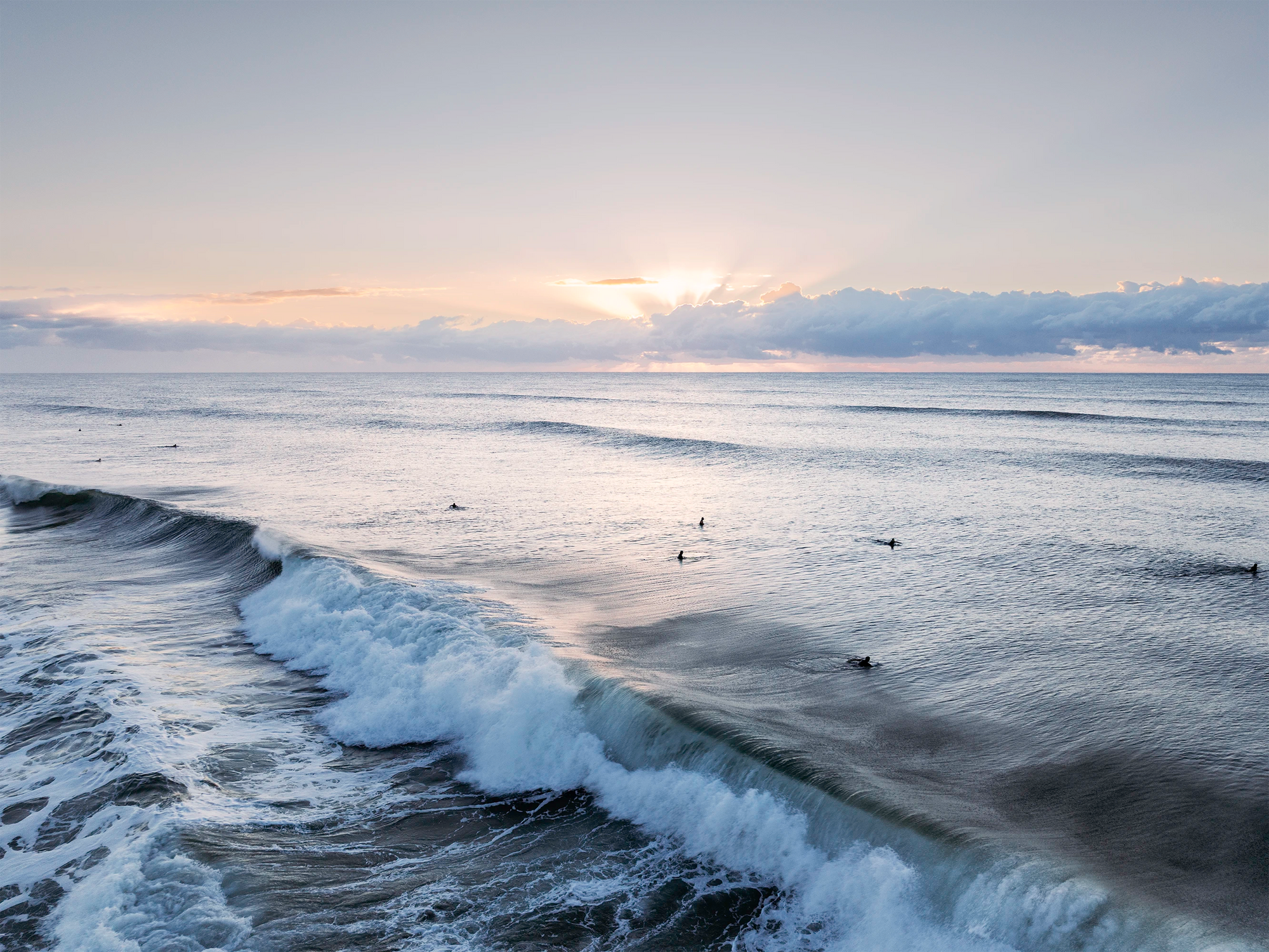 Surfers at Suffolk Park Beach, Byron Bay riding gentle waves in soft morning light along the Australian east coast.